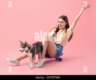 Süße Frau mit lustiger Husky-Welpe und Skateboard auf Farbhintergrund Stockfoto