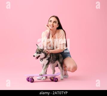 Süße Frau mit lustiger Husky-Welpe und Skateboard auf Farbhintergrund Stockfoto