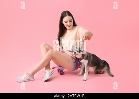 Süße Frau mit lustiger Husky-Welpe und Skateboard auf Farbhintergrund Stockfoto