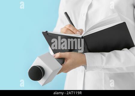 Journalist mit Mikrophon, der in Notizbuch vor Farbhintergrund schreibt Stockfoto
