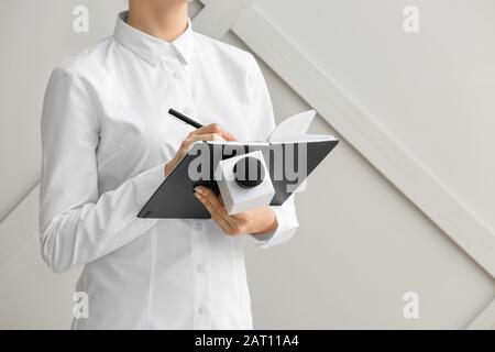Journalist mit Mikrofon, der vor grauem Hintergrund in Notizbuch schreibt Stockfoto