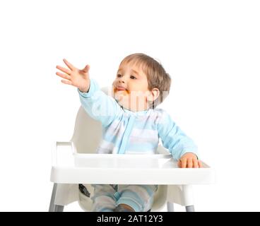 Süßer kleiner Junge mit verschmiertem Mund, der im Hochstuhl vor weißem Hintergrund sitzt Stockfoto