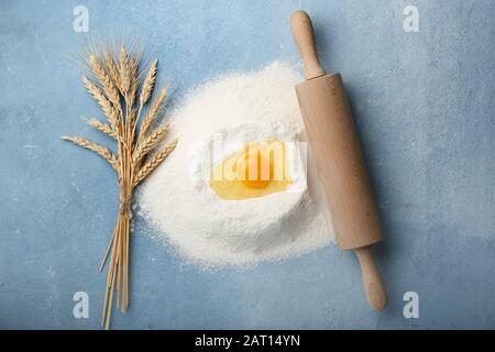 Mehl mit rohem Ei und Rollstift auf Farbhintergrund Stockfoto