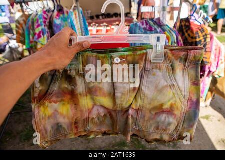 Nahaufnahme eines Paares gefärbter Shorts mit der Binde- und Farbstofftechnik. Im verschwommenen Hintergrund werden Produkte in einem Hippie-Geschäft auf dem lokalen Bauernmarkt verkauft. Stockfoto