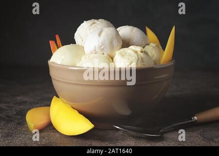 Schüssel mit schmackhaftem Eis und Mango auf dunklem Hintergrund Stockfoto