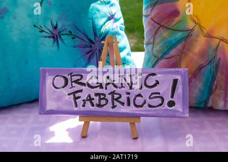 Handschriftlich unterzeichtes Schild, das auf einer Staffelei auf dem örtlichen Bauernmarkt ruht. Das Schild informiert über Produkte aus natürlichen und organischen Stoffen und Kleidungsstücken. Stockfoto