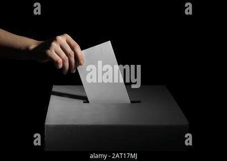 Wahlfrau in der Nähe der Wahlurne auf dunklem Hintergrund Stockfoto