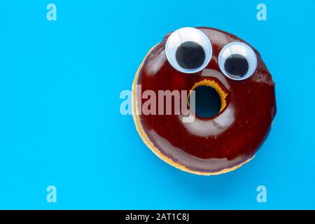 Ein Tim Hortons Chocolate Dip Donut mit Black Wiggle Googly Augballs auf blauem Hintergrund Stockfoto