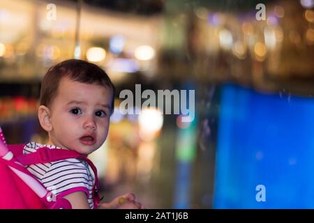 Ein süßes kleines Mädchen in einem Buggy in der Nacht in Dubai mit leuchtenden Lichtern von Straßenlampen im Hintergrund. Stockfoto