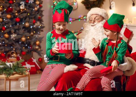 Weihnachtsmann und kleine elf Kinder Eröffnungsgeschenk im Zimmer, das zu Weihnachten dekoriert ist Stockfoto