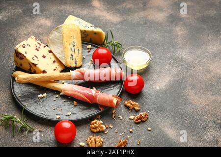 Teller mit frischem Käse, Honig und Snacks auf grauem Hintergrund Stockfoto