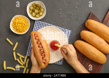 Frau, die leckeren heißen Hund und pommes frites am Tisch isst Stockfoto