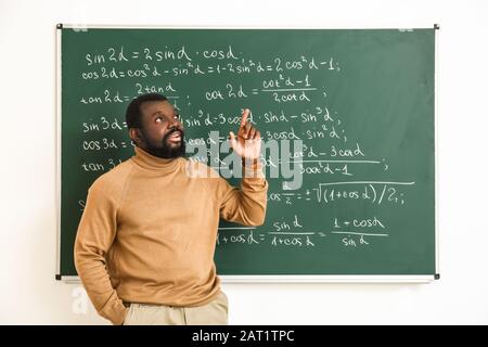 Afroamerikanischer Mathematiklehrer in der Nähe von Tafel im Klassenzimmer Stockfoto