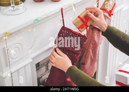 Frau, die Geschenke in Weihnachtssocken legt, die zu Hause am Kamin hängen Stockfoto