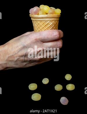 Die Hand der Frau hält einen Kegel voller Obstkäuze auf schwarzem Grund auf Stockfoto