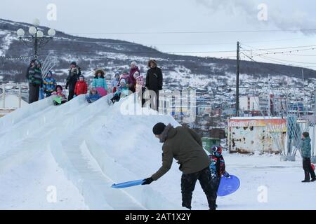 Magadan, Russland - Dezember 2019. Menschen auf der großen Eisrutsche aus Schnee. Winterurlaub. Kinder und ihre Eltern rutschen nach unten Stockfoto