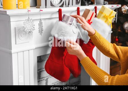 Frau, die Geschenke in Weihnachtssocken legt, die zu Hause am Kamin hängen Stockfoto