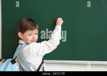 Kleiner Schuljunge, der im Klassenzimmer an der Tafel schreibt Stockfoto