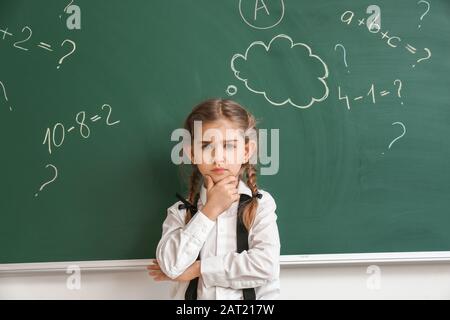 Nachdenkliches kleines Schulmädchen in der Nähe von Tafel im Klassenzimmer Stockfoto