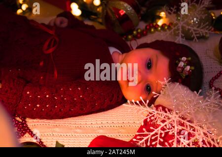 Ein süßes Mädchen in rotem Outfit an einem Heiligabend auf der weißen Decke. Stockfoto