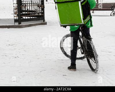 24-Stunden-Lieferservice von Cafés und Restaurants. Mitfahrkurier auf dem Fahrrad mit einem grünen isothermen Rucksack fährt schnell. Courier liefert Lebensmittel per Stockfoto