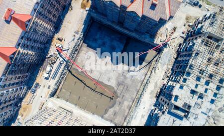 Bau einer mehrstöckigen Wohnanlage. Luftansicht. Betonfundament eines der Gebäude. Durch die Füllung wird die Betonpumpe hergestellt Stockfoto