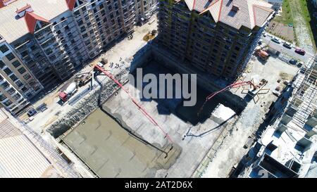 Bau einer mehrstöckigen Wohnanlage. Luftansicht. Betonfundament eines der Gebäude. Durch die Füllung wird die Betonpumpe hergestellt Stockfoto