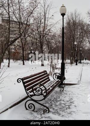 Leere rote Parkbänke im Schnee. Wintertag im Park. Schneit. Stockfoto