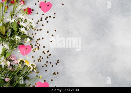 Grußkarte zum Valentinstag. Komposition mit Blumen, rosafarbenen Herzen und kleinen Sternen auf blauem Hintergrund. Platz in der Draufsicht für eine flache Textlage Stockfoto