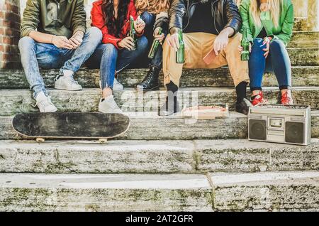 Eine Gruppe von Freunden, die Bier trinken und im Freien Pizza essen - Jugendliche, die im Treppenhaus sitzen und Spaß beim Musikhören haben - Freundschaft, Party, soc Stockfoto