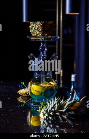 Herstellung von Hookah in der Ananas. Die geschnittene Ananas liegt in der Schüssel der Hookah. Runde Kapuzenflasche mit blauer Flüssigkeit. Hookah an Ananas. Stockfoto