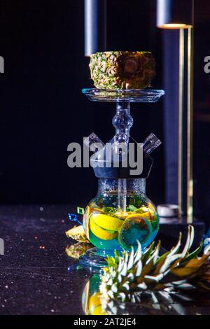 Herstellung von Hookah in der Ananas. Die geschnittene Ananas liegt in der Schüssel der Hookah. Runde Kapuzenflasche mit blauer Flüssigkeit. Hookah an Ananas. Stockfoto