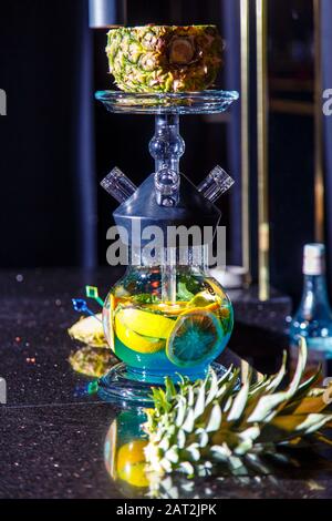 Herstellung von Hookah in der Ananas. Die geschnittene Ananas liegt in der Schüssel der Hookah. Runde Kapuzenflasche mit blauer Flüssigkeit. Hookah an Ananas. Stockfoto