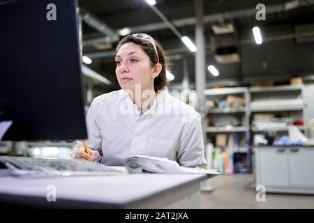 Frau in weißem Mantel sitzt am Tisch im Labor, verschwommener Hintergrund Stockfoto