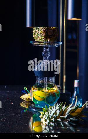 Herstellung von Hookah in der Ananas. Die geschnittene Ananas liegt in der Schüssel der Hookah. Runde Kapuzenflasche mit blauer Flüssigkeit. Hookah an Ananas. Stockfoto