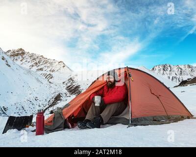 Ein bärtiger Mann reist im Winter in die Berge. Verbringen Sie die Nacht in einem Zelt. Stockfoto