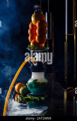 Hookah auf der Orange. Orange Hookah. Hookah mit einem runden durchsichtigen Kolben, in dem in Scheiben geschnittene Orangen und Minzblätter in roter Lauge schweben. Die Kapuzenbuge Stockfoto