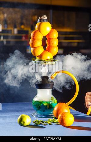 Hookah auf der Orange. Orange Hookah. Hookah mit einem runden durchsichtigen Kolben, in dem in Scheiben geschnittene Orangen und Minzblätter in roter Lauge schweben. Die Kapuzenbuge Stockfoto