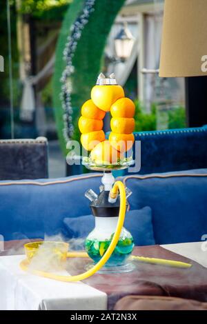Hookah auf der Orange. Orange Hookah. Hookah mit einem runden durchsichtigen Kolben, in dem in Scheiben geschnittene Orangen und Minzblätter in roter Lauge schweben. Die Kapuzenbuge Stockfoto