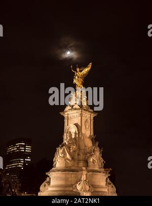 Niedriger Winkel Nachtansicht, Königin Victoria Gedenkstatue vom Buckingham Palace beleuchtet, isoliert in dunklem Himmel; Winged Victory Statue scheint in Mondlicht. Stockfoto