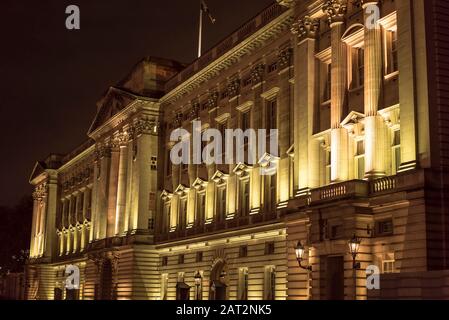 Abgewinkelte, detailgetreue Seitenansicht der berühmten Außenfassade des Buckingham Palace, die nachts am kalten Novemberabend beleuchtet wurde. Residenz des Königlichen Palastes. Stockfoto