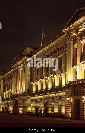 Abgewinkelte, detailgetreue Seitenansicht der berühmten Außenfassade des Buckingham Palace, die nachts am kalten Novemberabend beleuchtet wurde. Residenz des Königlichen Palastes. Stockfoto