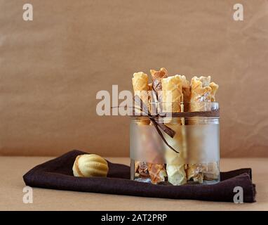 Hausgemachtes Backen. Köstliche Waffelrollen mit Puderzucker in einer Glasschale mit dekorativer Dekoration auf einer braunen Textilserviette auf einem Bastelpapier Stockfoto