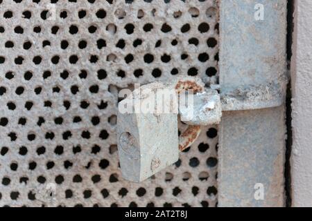 Eine Nahansicht einer verschlossenen, aus Metall vermaschten Tür, die zu einem Durchgang unter einem Gebäude führt. Mit Beton abgedeckt Stockfoto