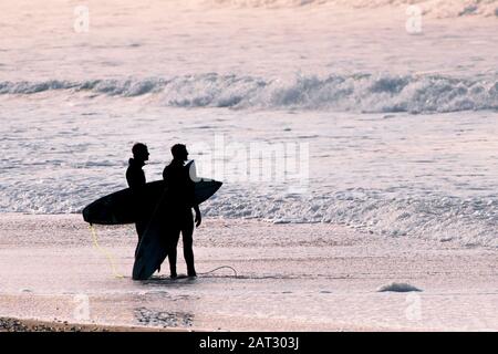 Surfer, die an der Küstenlinie stehen und die Meeresverhältnisse beim Abendlicht in Fistral in Newquay in Cornwall unter einen Blick sehen. Stockfoto