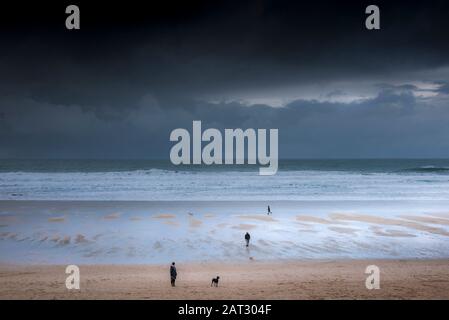 Hundegänger und ihre Haustiere am Fistral Beach, während dunkle Regenwolken Newquay in Cornwall nähern. Stockfoto