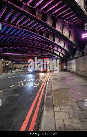 London/Großbritannien - 24. November 2019: Doppeldecker, die nachts die Bushaltestelle unter der Waterloo Bridge erreichen. Selektiver Fokus, Bus in Bewegung Stockfoto