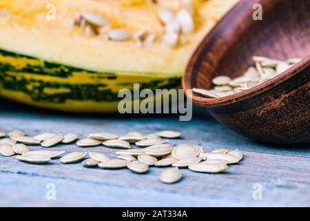 Kürbiskerne in einer Schüssel in der Nähe eines reifen Kürbisses auf blauen alten Bretter. Herbsternte. Stockfoto