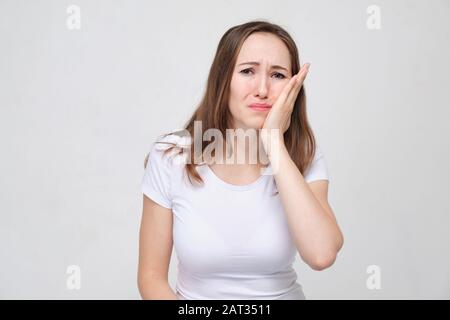 Ein Mädchen in einem weißen Hemd berührt ihre Wange mit der Hand. Zahnache-Konzept. Nahaufnahme. Stockfoto