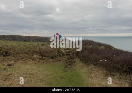 Female Walker Crossing a Stepping Stone Stile on the South West Coast Path Between Mullion Cove and Lizard Point in Rural Cornwall, England, Großbritannien Stockfoto